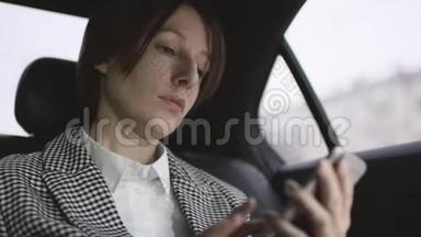 穿着白色上衣的棕色头发的漂亮女人，在车上检查外套，在手机上输入信息